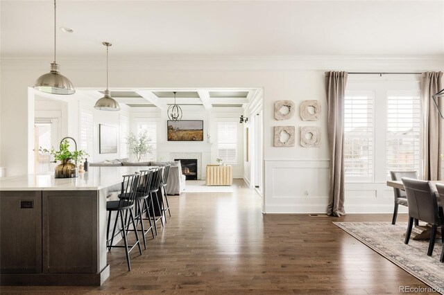 kitchen with ornamental molding, dark wood-style flooring, a kitchen breakfast bar, light countertops, and coffered ceiling