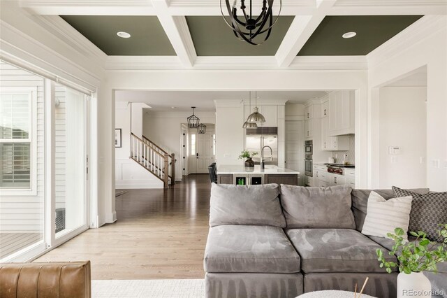living area with an inviting chandelier, light wood finished floors, ornamental molding, stairway, and coffered ceiling