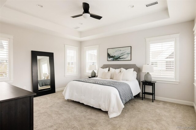 bedroom with light colored carpet, visible vents, multiple windows, and a raised ceiling