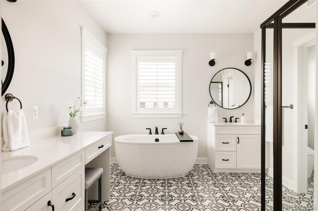 full bathroom featuring a freestanding tub, baseboards, two vanities, tile patterned floors, and a sink