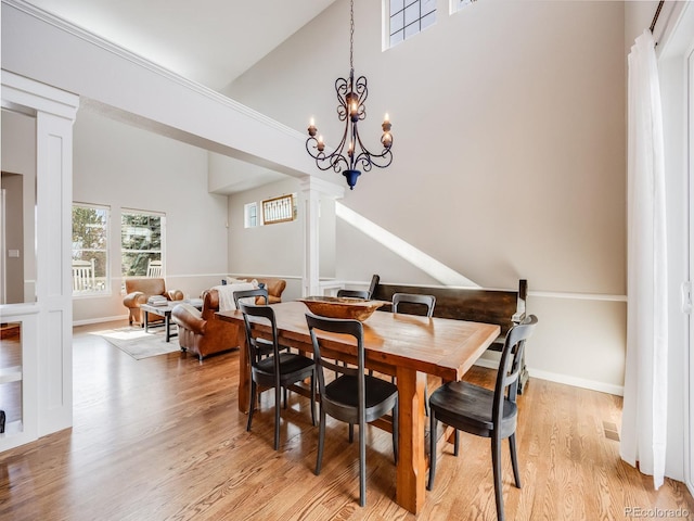 dining room with decorative columns, high vaulted ceiling, a notable chandelier, and light wood-type flooring