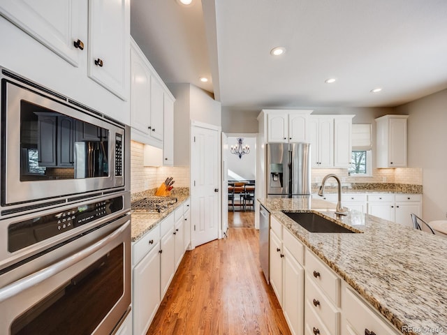 kitchen featuring appliances with stainless steel finishes, white cabinetry, sink, backsplash, and light wood-type flooring