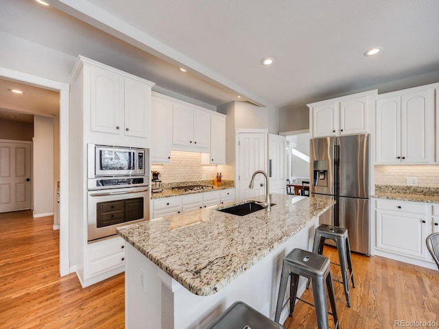 kitchen with stainless steel appliances, white cabinetry, sink, and a center island with sink