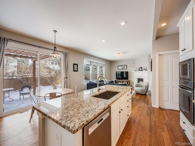 kitchen with sink, white cabinetry, hanging light fixtures, stainless steel appliances, and a kitchen island with sink