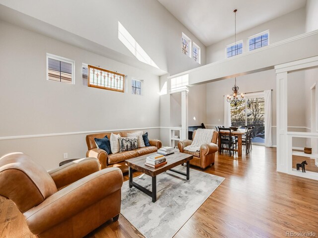 living room featuring hardwood / wood-style flooring, a towering ceiling, a chandelier, and decorative columns