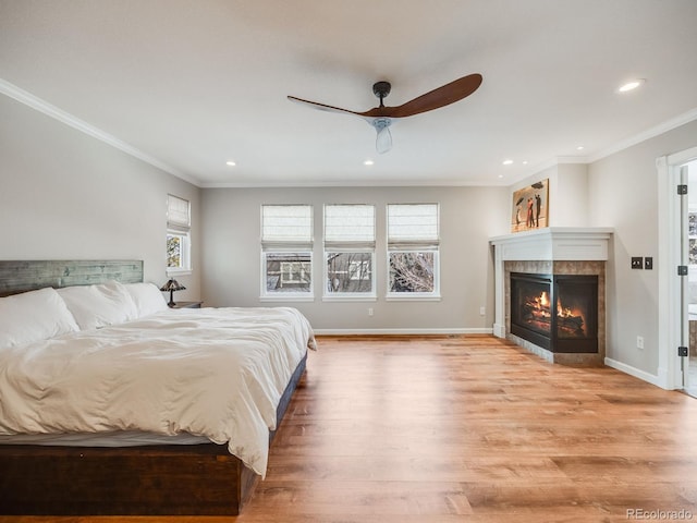 bedroom featuring a tiled fireplace, light hardwood / wood-style flooring, ornamental molding, and ceiling fan