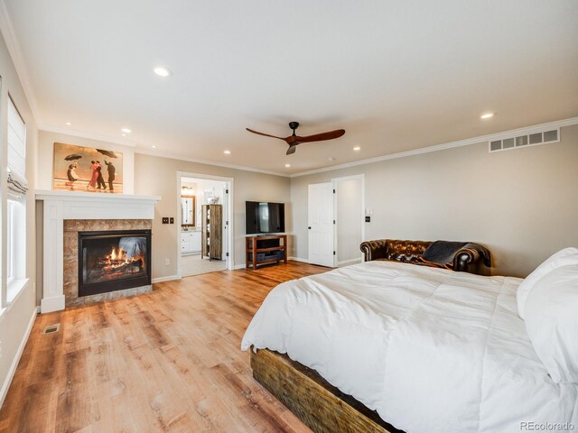 bedroom with crown molding, ceiling fan, ensuite bathroom, light hardwood / wood-style floors, and a tiled fireplace