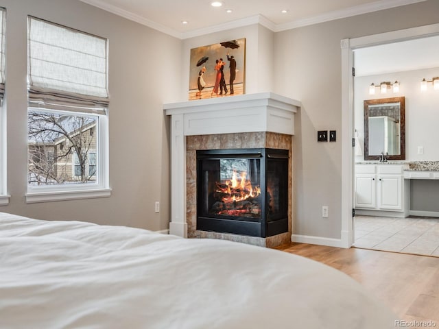 bedroom with a tile fireplace, ensuite bathroom, sink, ornamental molding, and light hardwood / wood-style floors