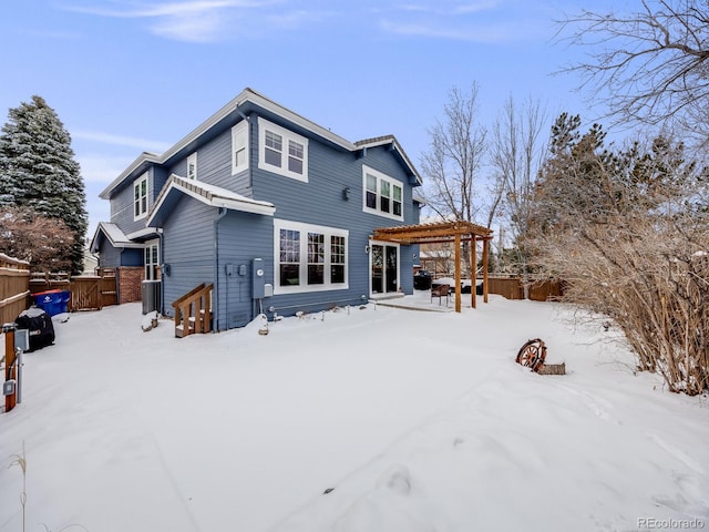 snow covered back of property with a pergola