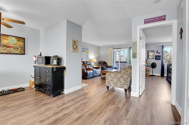 living room featuring ceiling fan, a textured ceiling, a wealth of natural light, and light hardwood / wood-style flooring