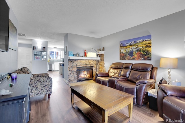 living room with a stone fireplace, hardwood / wood-style floors, and a textured ceiling