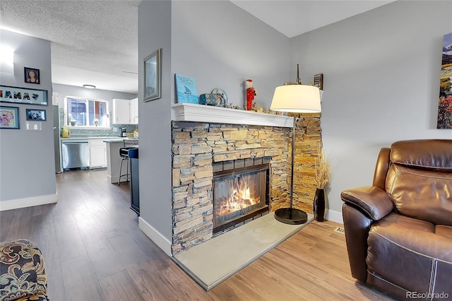 living room featuring a textured ceiling, hardwood / wood-style flooring, and a stone fireplace