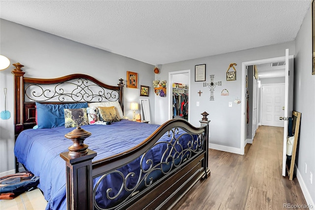 bedroom with a walk in closet, wood-type flooring, a textured ceiling, and a closet