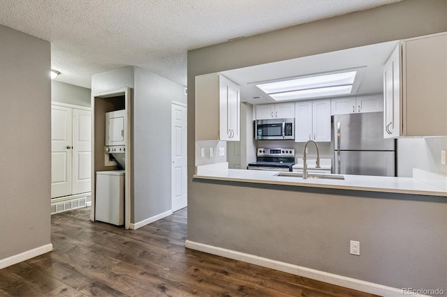 447 S Memphis Way Unit 7, Aurora, CO 80017 - kitchen with appliances with stainless steel finishes, stacked washer / dryer, dark wood-type flooring, white cabinets, and a peninsula