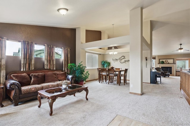 living room with a tiled fireplace, ceiling fan with notable chandelier, baseboards, and carpet