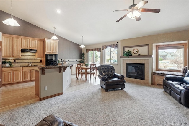 living area with light carpet, high vaulted ceiling, ceiling fan, and a tiled fireplace