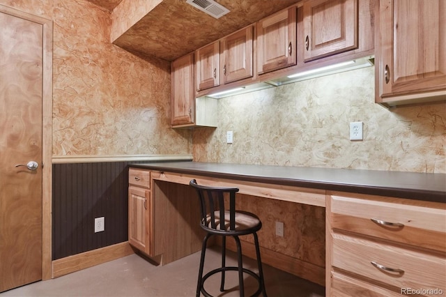 kitchen with visible vents, wallpapered walls, built in desk, dark countertops, and a kitchen breakfast bar