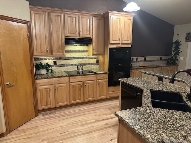 kitchen with tasteful backsplash, under cabinet range hood, light wood-type flooring, black appliances, and a sink