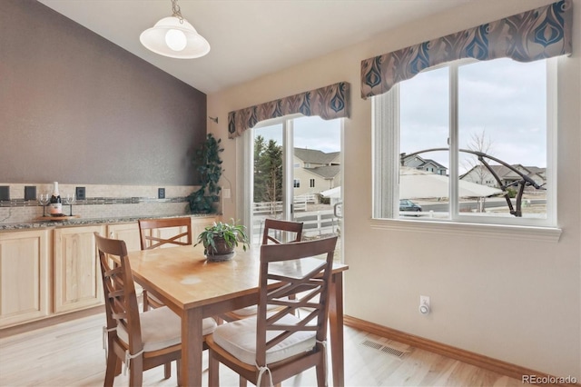 dining area with visible vents, baseboards, light wood-style floors, and vaulted ceiling