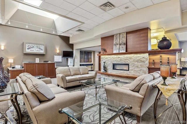 living room featuring a stone fireplace, a drop ceiling, and carpet floors