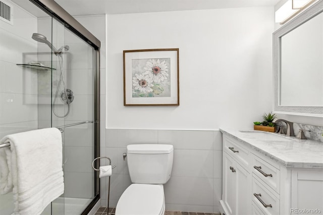 bathroom featuring a shower with door, vanity, tile walls, and toilet