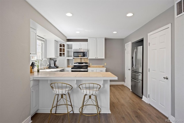 1343 Valentia St, Denver, CO 80220 - kitchen with appliances with stainless steel finishes, a peninsula, a kitchen breakfast bar, white cabinets, and recessed lighting