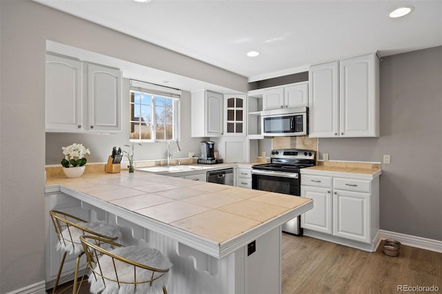 1343 Valentia St, Denver, CO 80220 - kitchen with stainless steel appliances, a kitchen bar, a peninsula, baseboards, and white cabinetry
