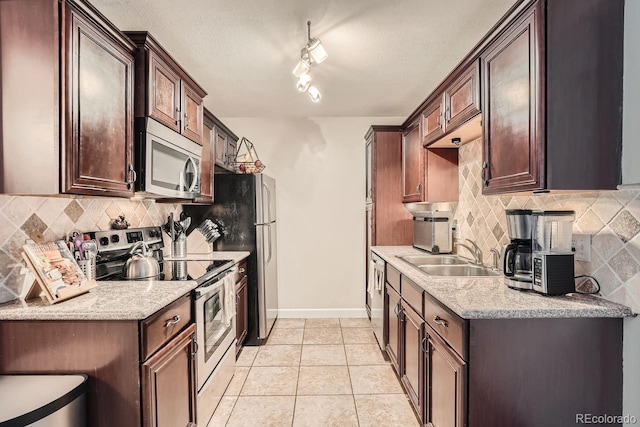 kitchen featuring sink, backsplash, track lighting, light tile patterned floors, and appliances with stainless steel finishes