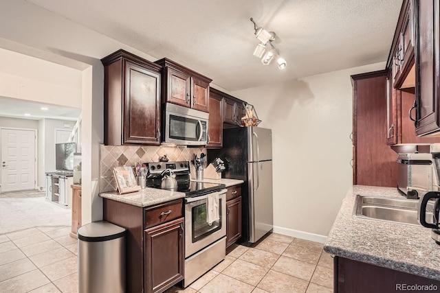 kitchen with backsplash, rail lighting, light stone countertops, light tile patterned floors, and appliances with stainless steel finishes