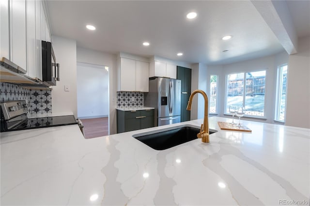 kitchen with appliances with stainless steel finishes, backsplash, white cabinetry, and light stone counters