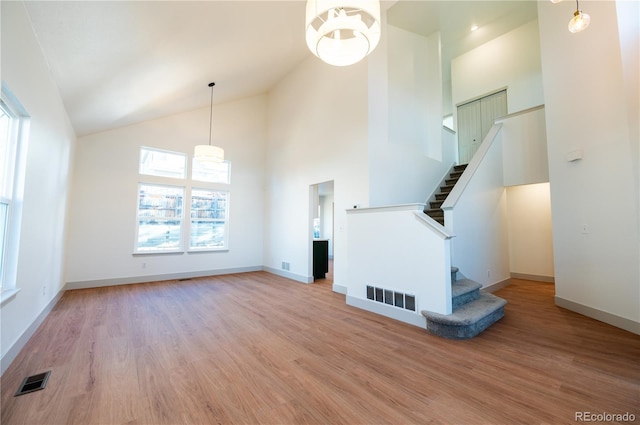 unfurnished living room with a chandelier, high vaulted ceiling, and light hardwood / wood-style floors