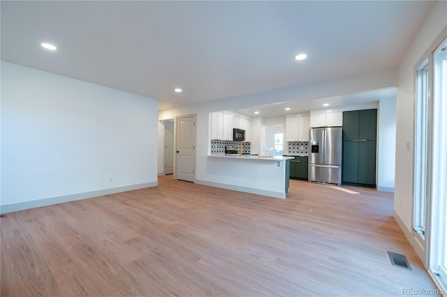 kitchen with light hardwood / wood-style flooring, backsplash, kitchen peninsula, stainless steel fridge, and white cabinets