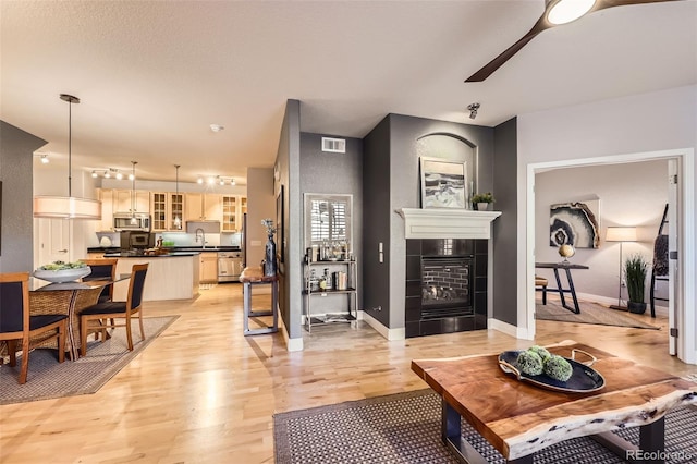 living room with light wood-type flooring, a tiled fireplace, sink, and ceiling fan