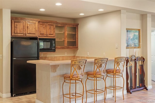 kitchen with kitchen peninsula, light tile patterned floors, black appliances, and a breakfast bar