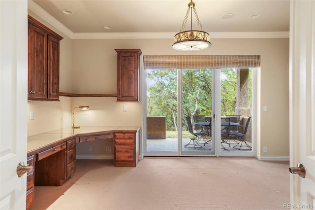 unfurnished office with crown molding, built in desk, and light colored carpet