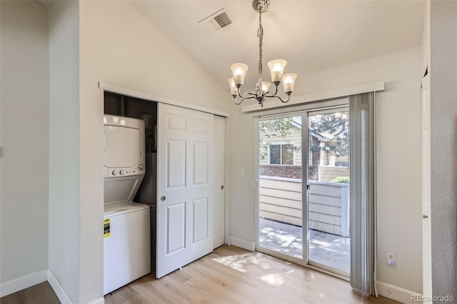 washroom featuring a notable chandelier, stacked washer / dryer, and light wood-type flooring