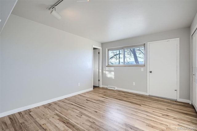 unfurnished bedroom with track lighting, light wood-type flooring, baseboards, and visible vents