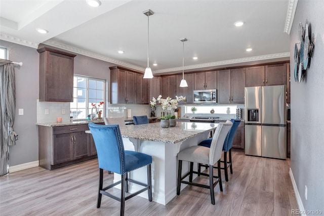 kitchen featuring a kitchen island, light stone countertops, pendant lighting, light wood-type flooring, and appliances with stainless steel finishes