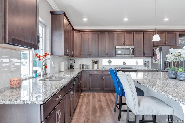 kitchen with appliances with stainless steel finishes, sink, light wood-type flooring, pendant lighting, and crown molding