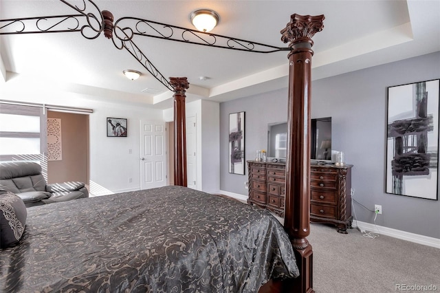 carpeted bedroom featuring ornate columns and a tray ceiling