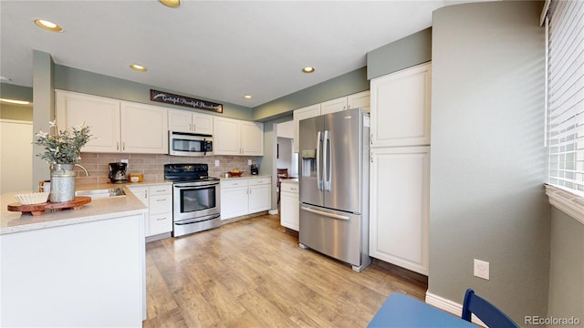 kitchen featuring sink, appliances with stainless steel finishes, decorative backsplash, white cabinets, and light wood-type flooring