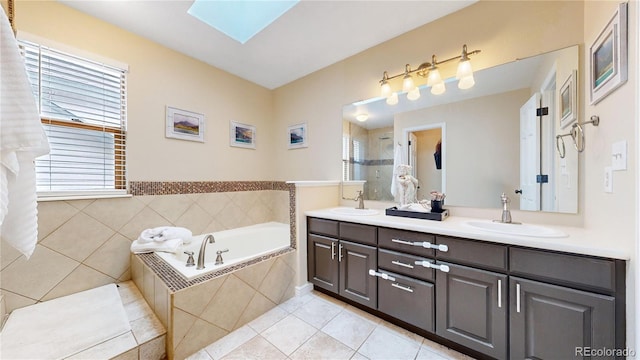 bathroom with tile patterned floors, a skylight, vanity, and a relaxing tiled tub