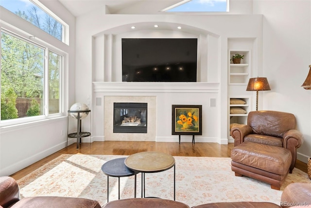 living area featuring built in features, a towering ceiling, wood finished floors, a fireplace, and baseboards