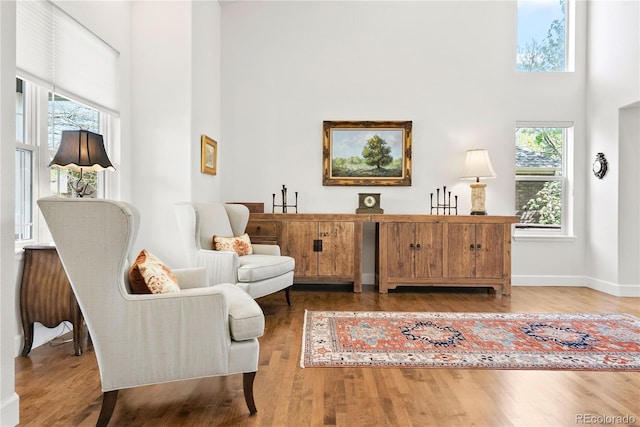 sitting room with baseboards, wood finished floors, and a towering ceiling