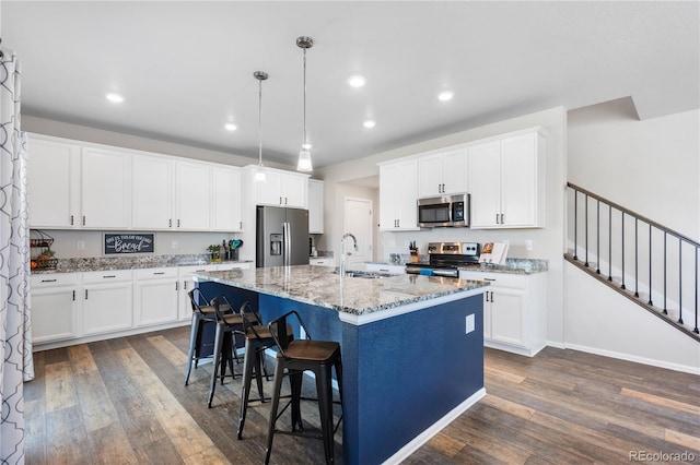 kitchen with appliances with stainless steel finishes, pendant lighting, white cabinetry, sink, and a center island with sink