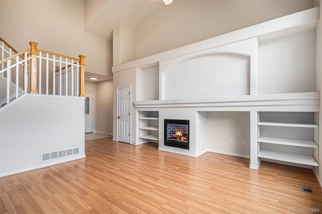 11862 W Stanford Pl, Morrison, CO 80465 - unfurnished living room featuring high vaulted ceiling, wood finished floors, baseboards, stairway, and a glass covered fireplace