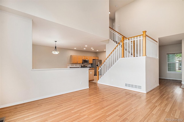 11862 W Stanford Pl, Morrison, CO 80465 - unfurnished living room with light wood-style floors, stairs, baseboards, recessed lighting, and a towering ceiling
