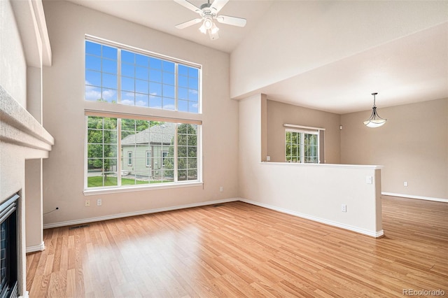 11862 W Stanford Pl, Morrison, CO 80465 - unfurnished living room featuring light wood-style flooring, baseboards, a fireplace, a ceiling fan, and a high ceiling