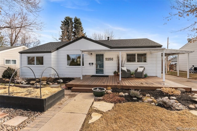 ranch-style home featuring a carport, roof with shingles, a deck, and a vegetable garden