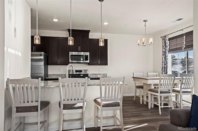 kitchen with dark wood-type flooring, hanging light fixtures, a breakfast bar area, light stone countertops, and appliances with stainless steel finishes